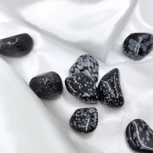 Rumpuhiottuja lumihiutaleobsidiaanikiviä valkoisella silkkikankaalla