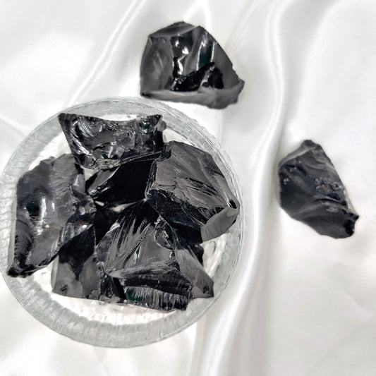 Obsidiaani raakapalat lasikulhossa ja valkoisen kankaan päällä