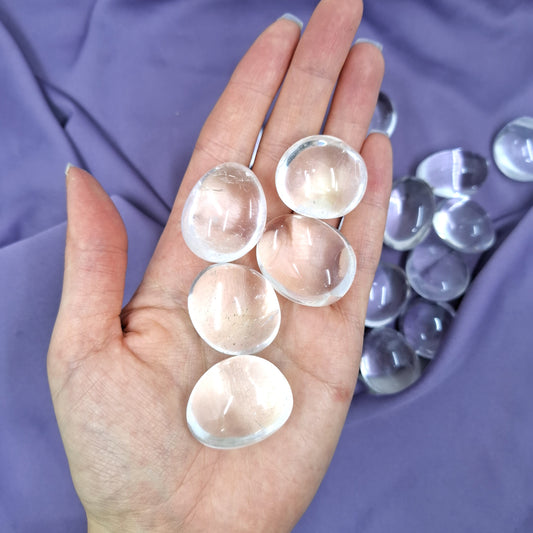 Läpinäkyvät rumpuhiotut vuorikristallit kädessä violetilla taustalla