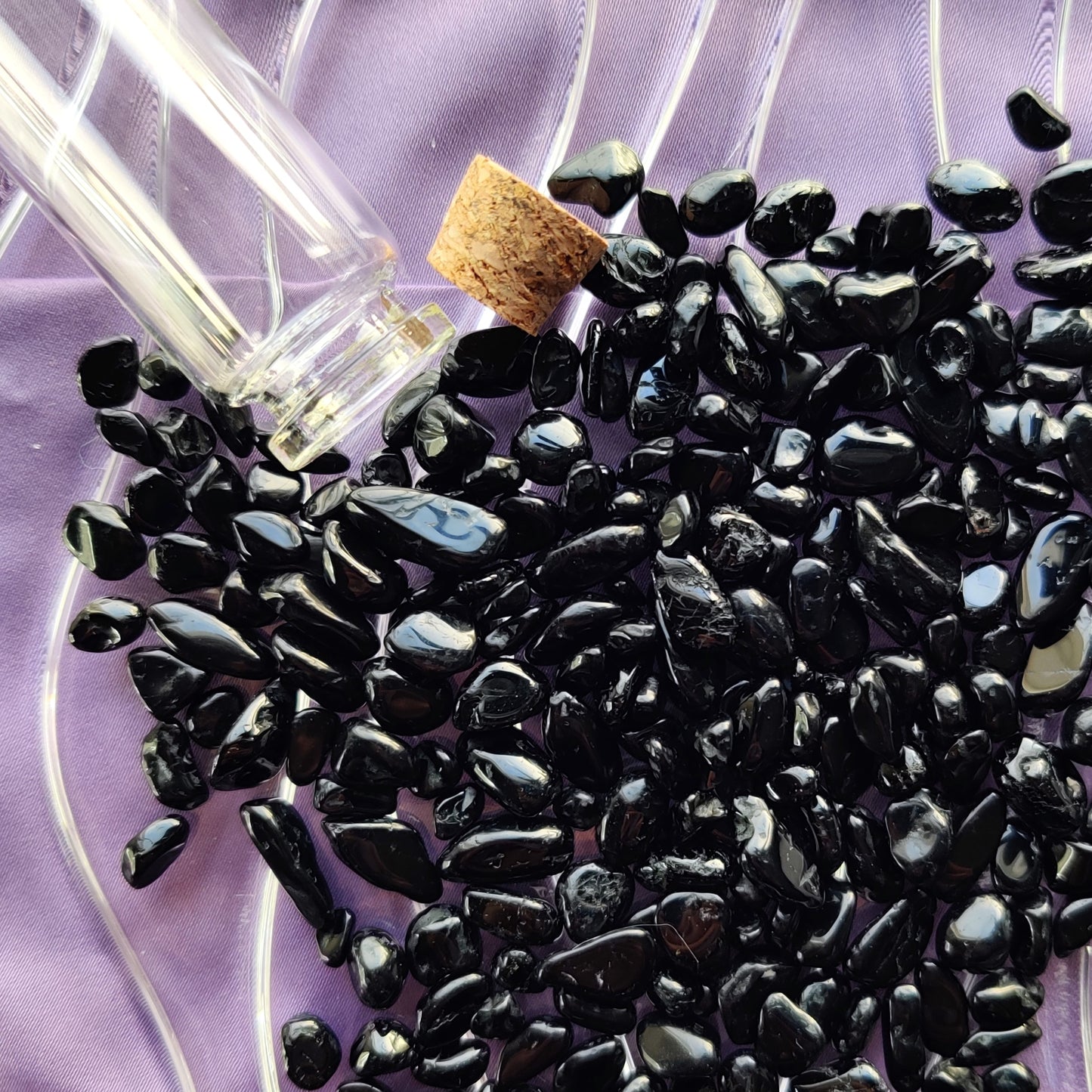 Musta turmaliini kristallihippua kuvattuna läheltä violetilla taustalla vieressään "loitsupullo" korkki auki