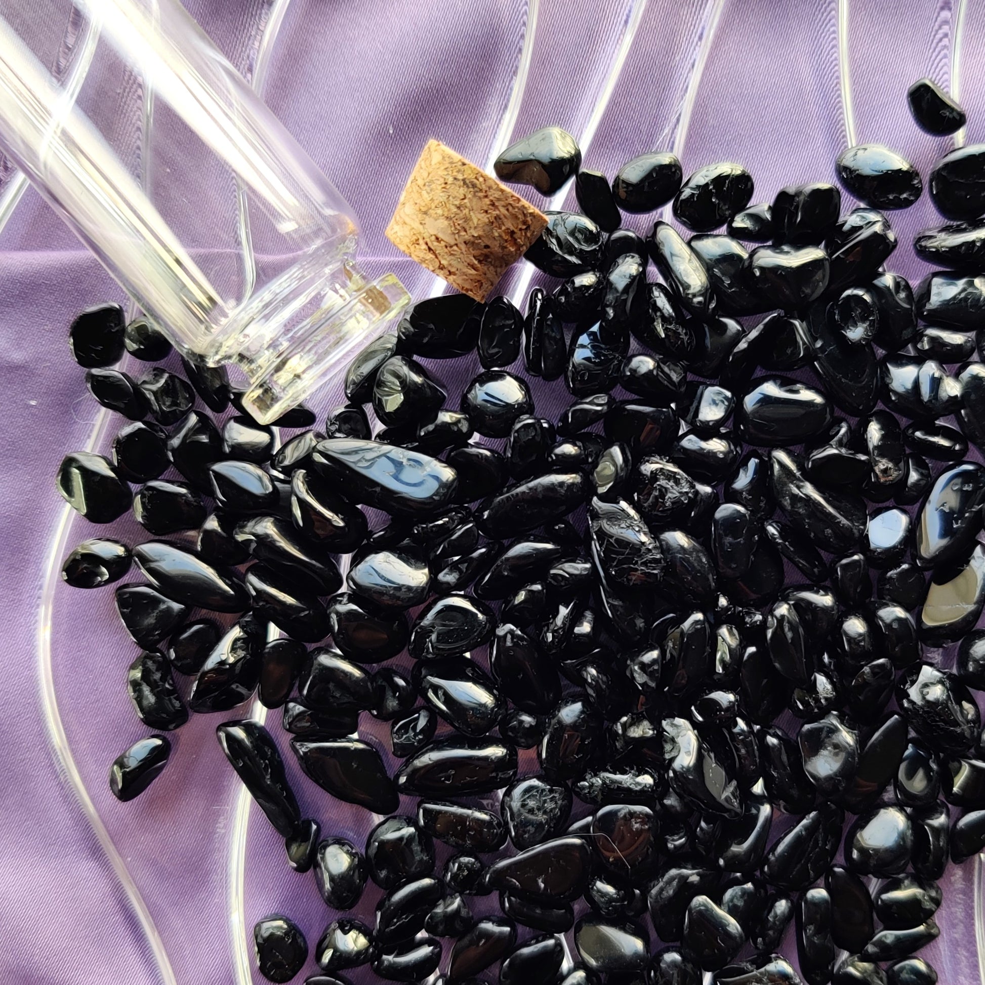 Musta turmaliini kristallihippua kuvattuna läheltä violetilla taustalla vieressään "loitsupullo" korkki auki