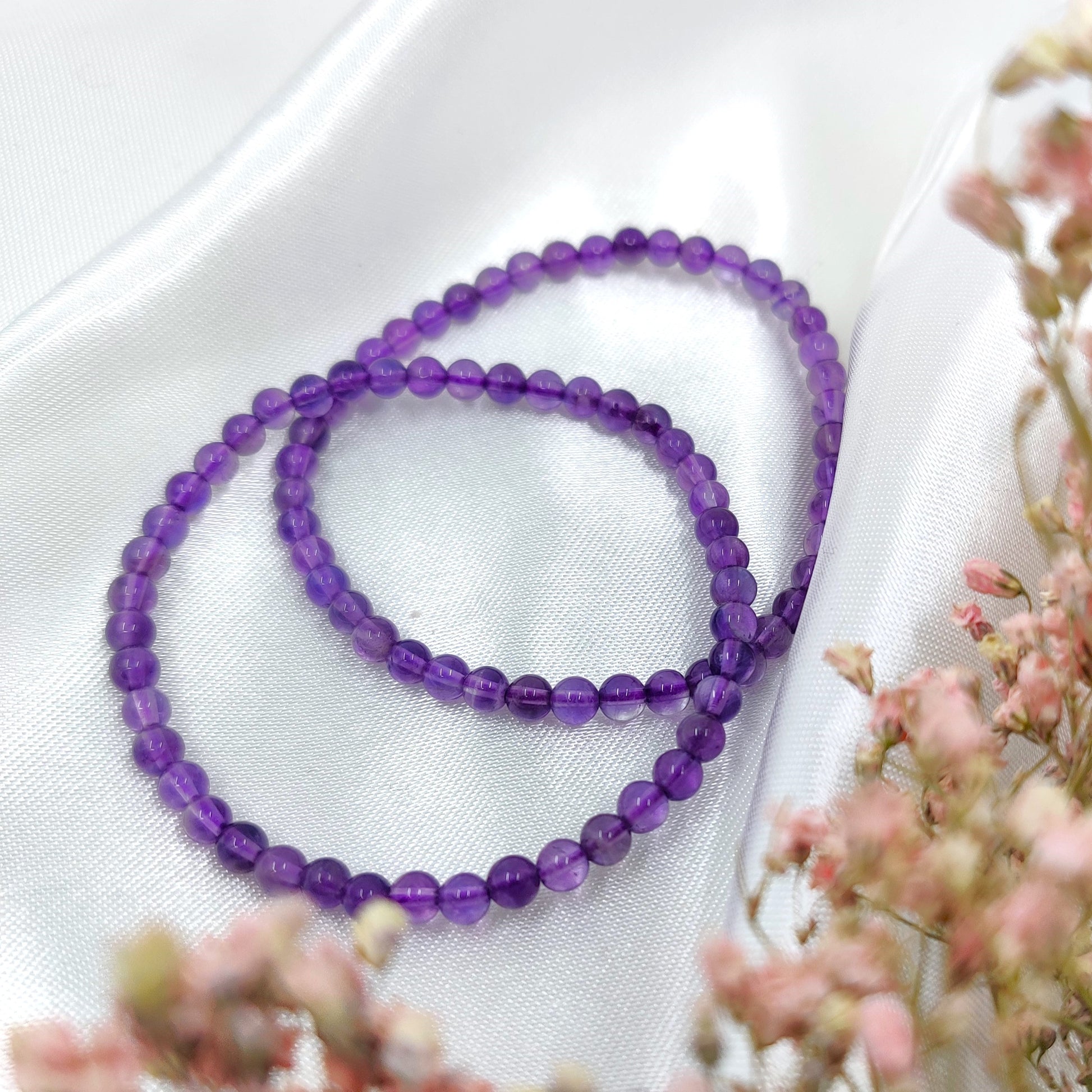 Violetti ametisti helmirannekoru valkoisen silkkikankaan päällä