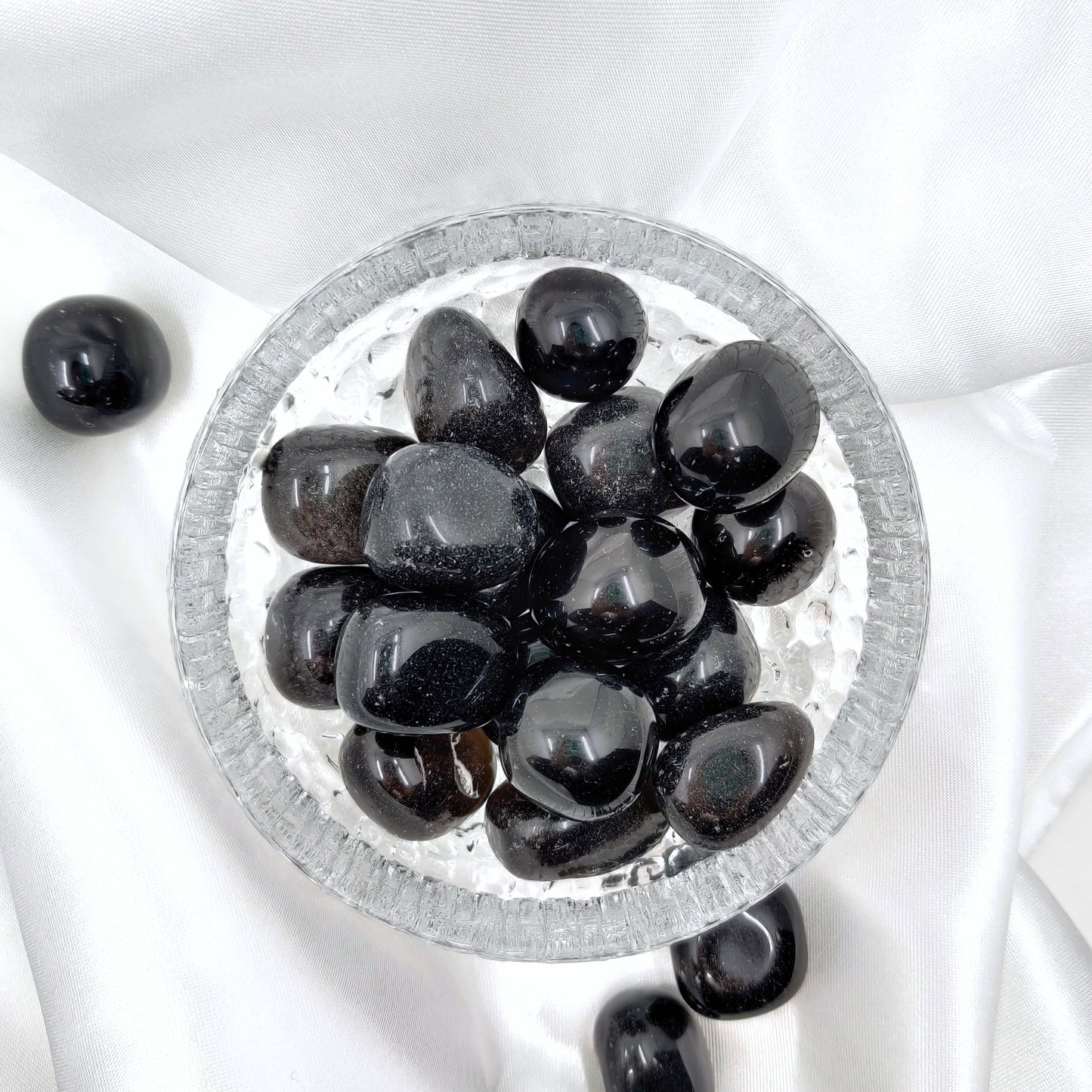 Hiottuja obsidiaaneja lasikulhossa valkoisella silkkikankaalla