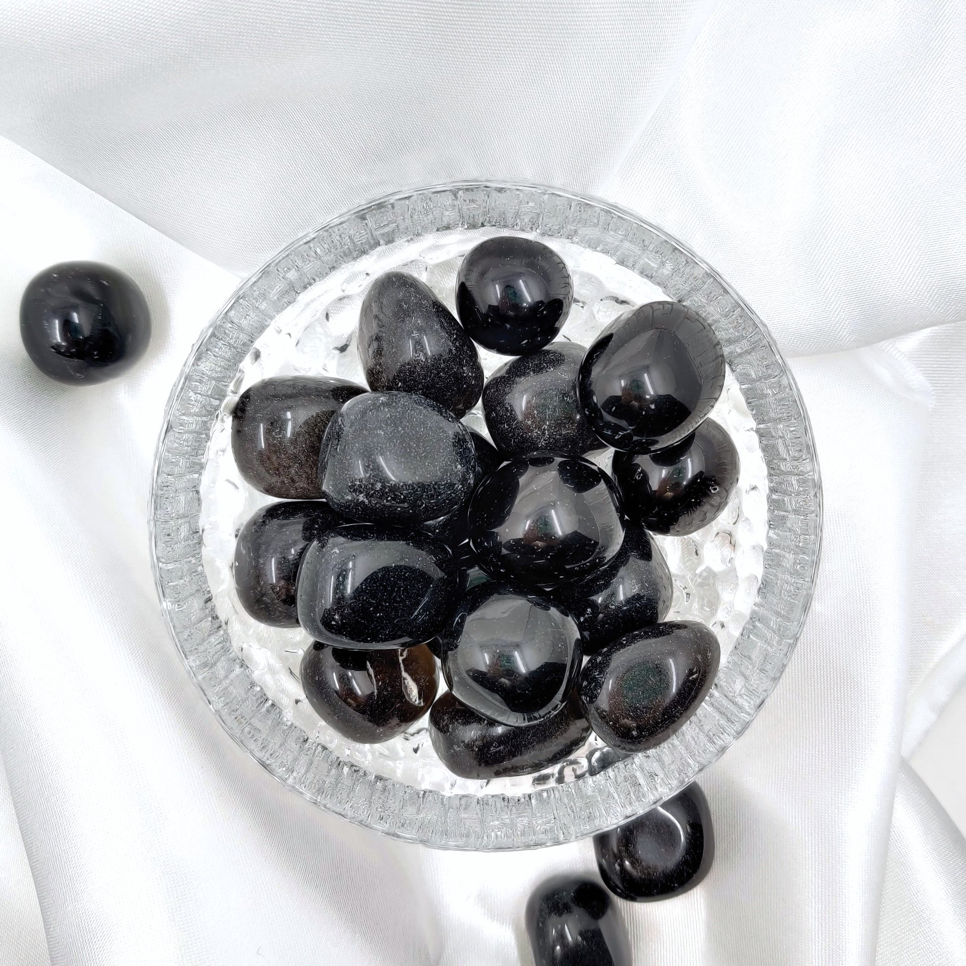 Hiottuja obsidiaaneja lasikulhossa valkoisella silkkikankaalla